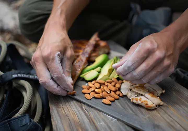 Close-up of a climber's hands preparing a ketogenic meal of avocado and chicken, representing the low-carbohydrate diet spectrum.