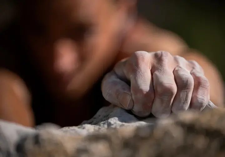 An extreme close-up of a climber's fingers in a stressful crimp grip, showing the immense force and tension on the finger pulleys that can lead to injury.