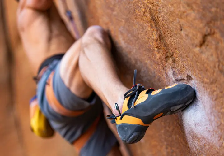 A close-up view of a climber's leg executing a secure heel-hook, showing the biomechanics and technique of the crux move.