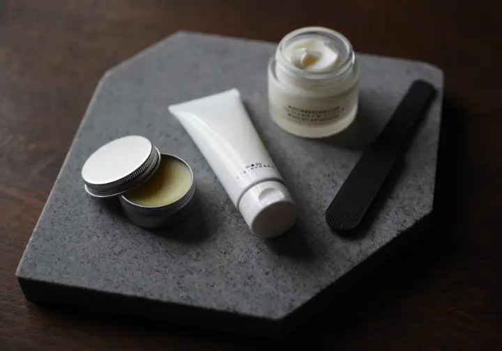 An overhead view of a selection of climbing skin care products, including balms, creams, and tools, neatly arranged on a natural rock surface.