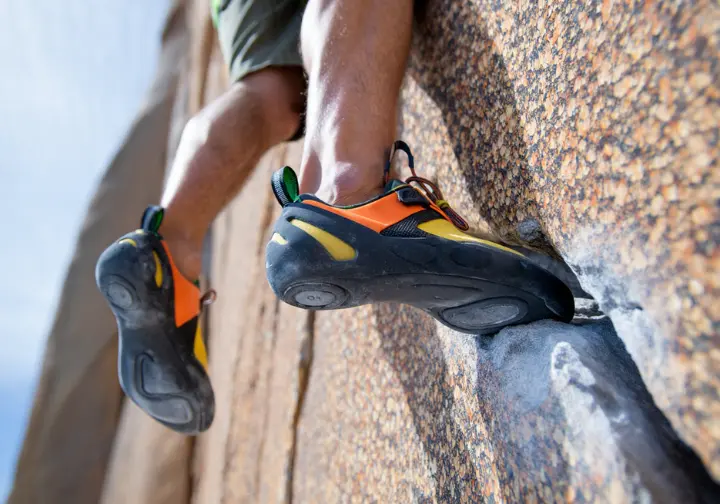 A close-up of a climber's feet in specialized, aggressive climbing shoes, demonstrating precision on tiny footholds on a vertical rock wall.