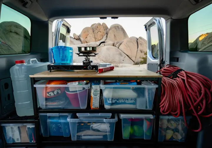 The organized interior of a climber's van, showing a strategic toolkit for resource management with a view of a mountain landscape out the back.