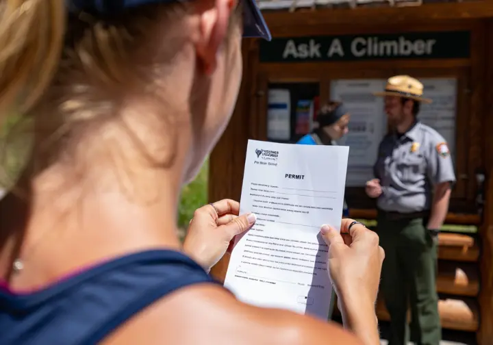 A climber carefully reviews an official Yosemite National Park wilderness climbing permit, highlighting the process of navigating the park's rules.