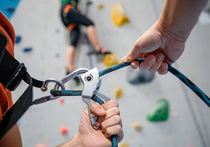A close-up of a belayer's hands safely managing the rope with a belay device, illustrating practical risk mitigation for a pregnant climber.