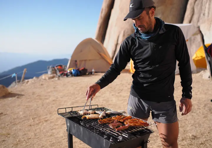 A climber at a campsite grills meat and fish, representing the all-animal-product approach of the carnivore diet.