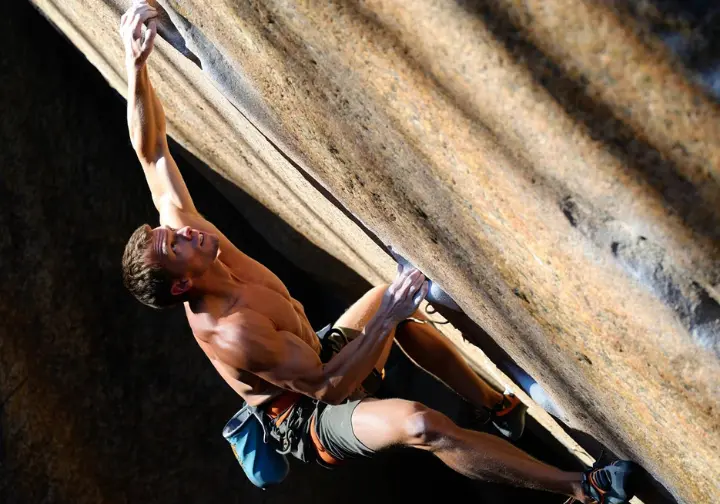 A strong climber executes a difficult move on an outdoor boulder, showcasing the performance gains achieved from a dedicated training board regimen.