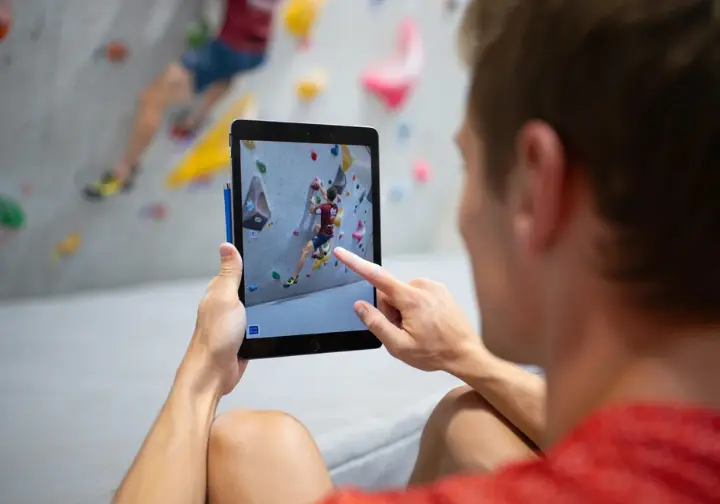 A climber analyzes their climbing technique using video review on a tablet to identify tactical flaws and improve their movement.