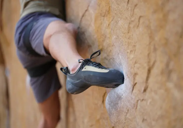 A close-up view of a climber performing a core technique, placing the inside edge of their shoe precisely on a small rock hold.