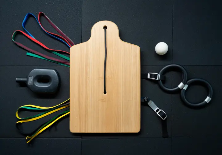 A flat-lay image of expert rock climbing workout equipment, including a hangboard, resistance bands, and grip trainers.