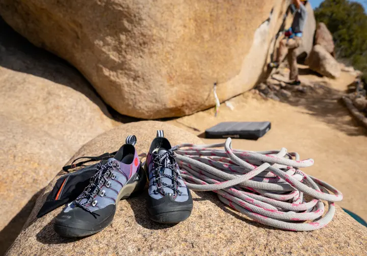 A pair of hybrid approach shoes, the solution for hiking and climbing, sit next to a rope and chalk bag at a climbing crag.