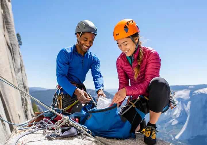 Two climbers practice Leave No Trace ethics by packing out all waste at a belay station in Yosemite, showing respect for the environment.