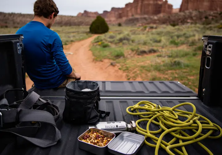 A climber organizes gear and food at the crag, showing the direct application of a fueling strategy for bouldering, sport, or trad climbing.