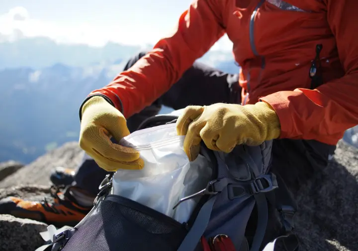 A climber demonstrates a responsible climbing ethic by carefully packing out their waste in a WAG bag in a pristine mountain environment.