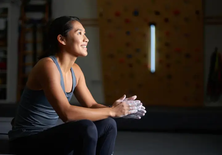 A climber sits peacefully on a crash pad, looking up with satisfaction at her fully built home training board, ready to begin her workout.