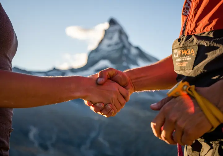 A close-up of a climber and a guide shaking hands, symbolizing the confident decision to hire a guide for the Matterhorn.