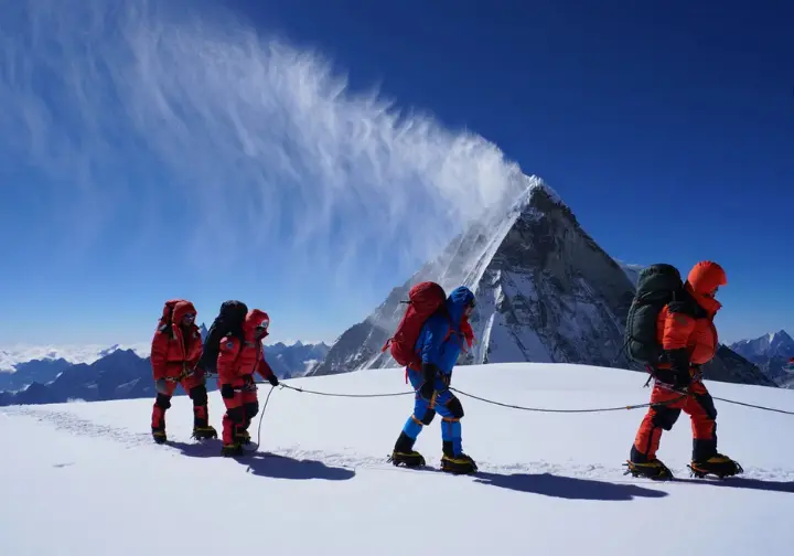 A team of climbers in the Himalayas observes a massive plume of snow being blown off a distant summit by the powerful jet stream, a characteristic weather pattern of the range.