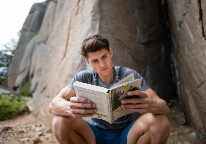 A climber studies a guidebook at a crag, representing the deconstruction of anecdotes by relying on factual evidence.