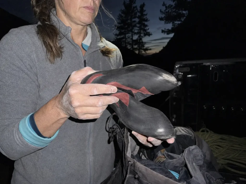 Aggressive downturned climbing shoes pulled from a pack at dusk, smooth tread-less rubber soles