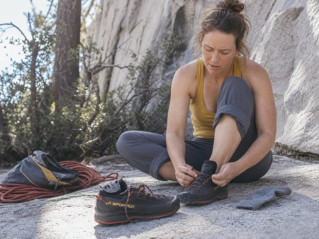 Climber lacing an approach shoe on a granite ledge, checking fit and heel lock before the walk-in