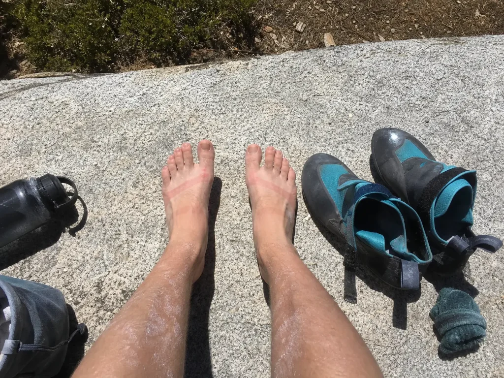 Bare feet resting on warm granite beside climbing shoes taken off between routes at the crag