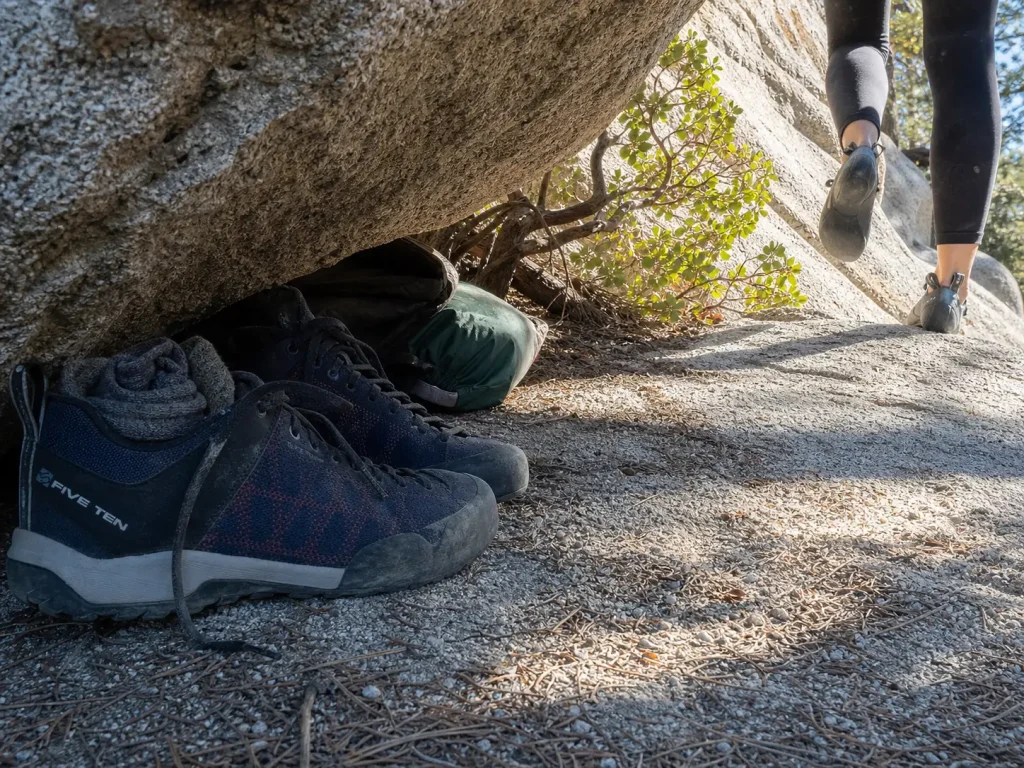 Approach shoes stashed under a boulder at the base of a climb during a crag day shoe swap