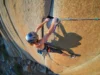 Aid Climbing Guide: A0-A5 Grades & Gear Explained A climber in full aid gear, including a helmet and harness, stands in aiders high on a sheer granite cliff, reaching up to place protection.