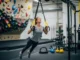 Key Principles: 4-Week Intro Strength Plan for Climbers A full-body view of a female climber performing an inverted row with a suspension trainer in a climbing gym's fitness area.
