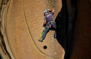 Complete Climbing Rope Guide: Single, Half, Twin, and Static A full-body shot of a climber in a helmet leading a sport climb on a sunny day, with the climbing rope visible below.