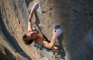 Low-Carb Carnivore Diet for Climbers: The Complete Guide A full-body shot of a rock climber in the middle of a difficult move on a sunny, overhanging cliff, showcasing the concept of power-to-weight ratio.