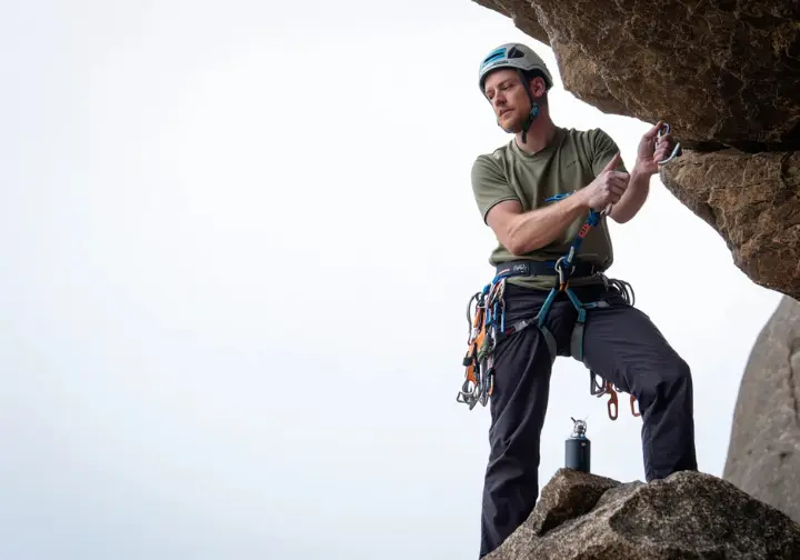 Full-body shot of a climber in a helmet carefully bounce-testing a gear placement on a rock face to assess its security and danger.