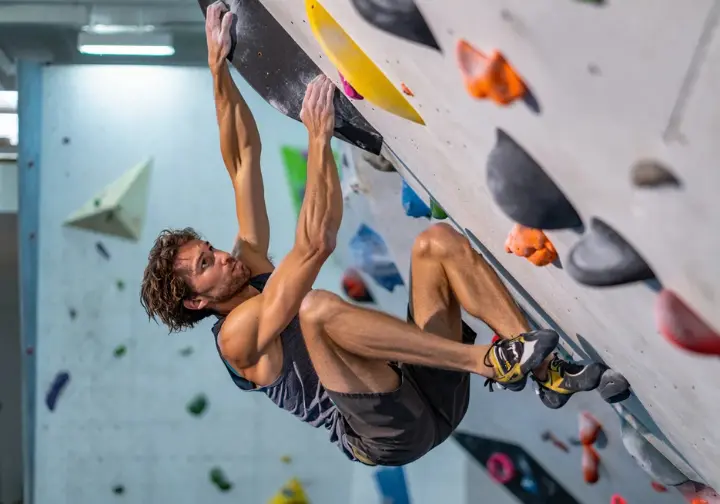 A lean climber is captured in a full-body shot as they fall from a powerful bouldering move, illustrating the paradox that a lighter body doesn't always mean better climbing performance.