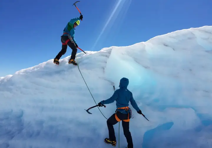 Two alpinists, seen in a full-body shot, are simul-climbing rapidly up a huge ice face on Mount Robson, connected by a long rope.