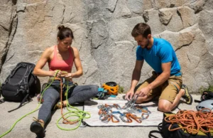 The Ultimate Climbing Gear Lifespan & Tracking System A fit couple in their late 20s inspecting their climbing rope and gear at the base of a sunny cliff before climbing.