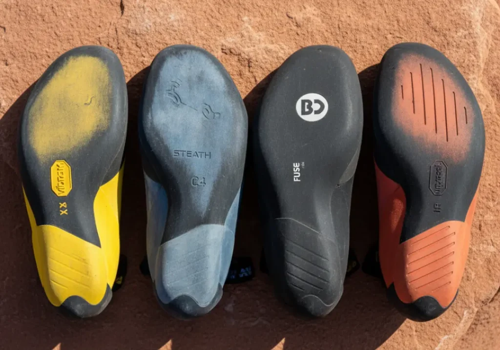 A top-down view of four different climbing shoe soles laid out on a rock slab for a direct comparison of their rubber compounds and designs.