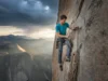 Dry vs Non-Dry Rope: A Data-Backed Performance Analysis A fit male climber in his late 20s managing a partially wet climbing rope at a multi-pitch belay station on a granite cliff face under dramatic skies.