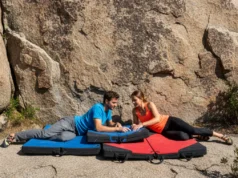 How to Choose a Crash Pad: An Expert Framework A fit couple in their late 20s wearing modern climbing apparel, arranging bouldering crash pads at the base of a sunny boulder.