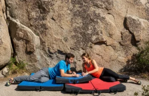 How to Choose a Crash Pad: An Expert Framework A fit couple in their late 20s wearing modern climbing apparel, arranging bouldering crash pads at the base of a sunny boulder.