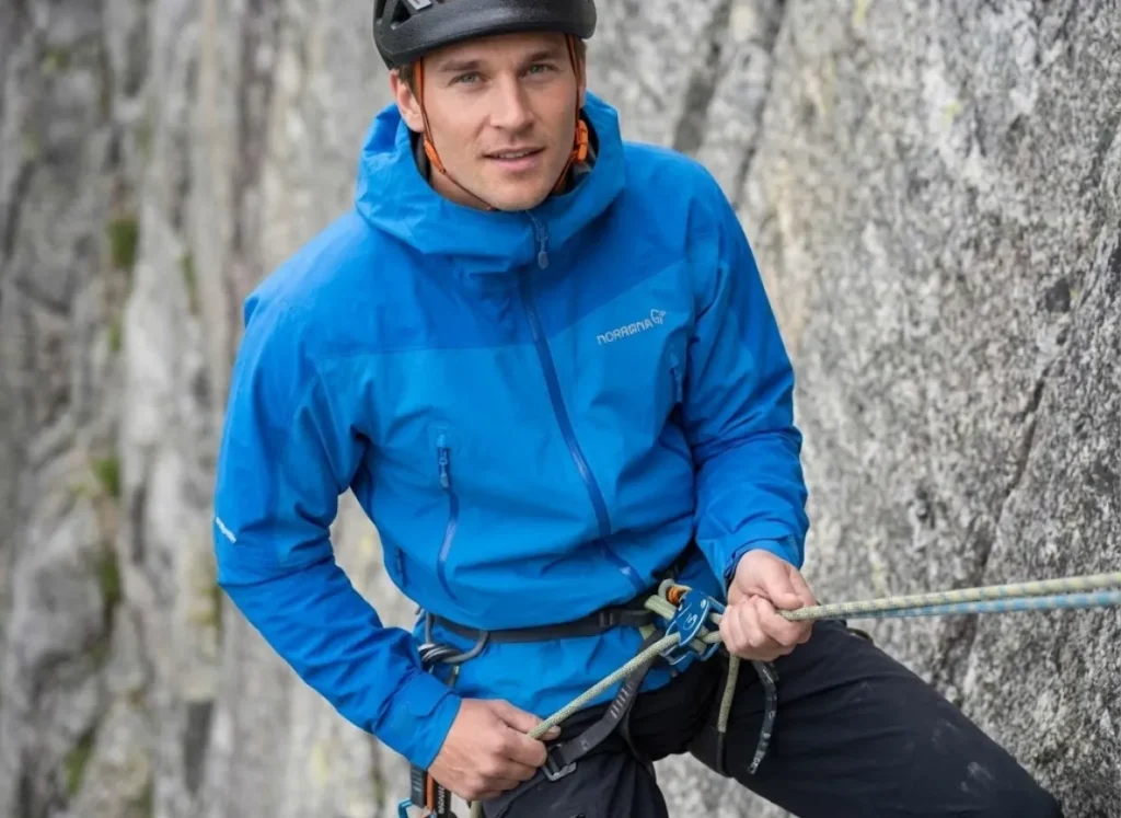 Climber performing a weight test on the rappel system, fully loading the device while still backup-tethered to the anchor, demonstrating the BRAKES protocol.