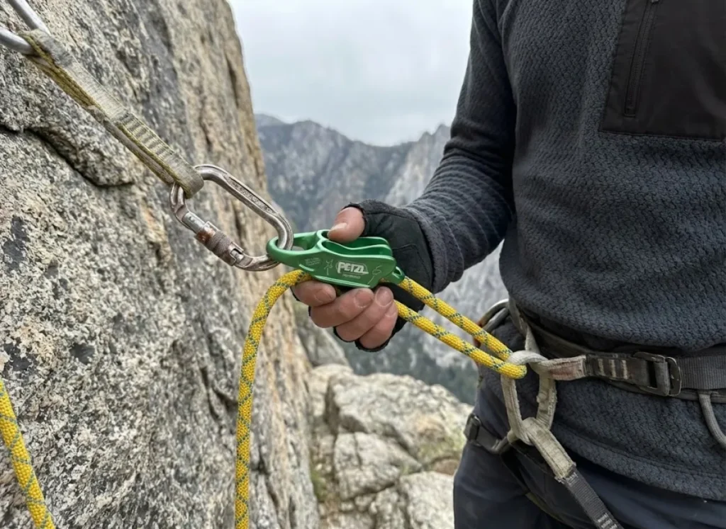 Climber checking a Petzl Reverso belay device and Sterling rope setup before rappelling.