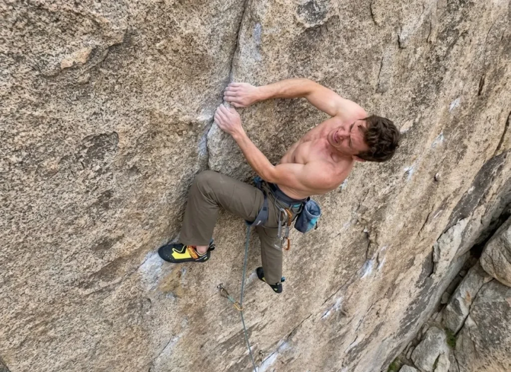 Rock climber in Scarpa shoes and Prana pants struggling with inefficient chicken wing form on a granite wall.