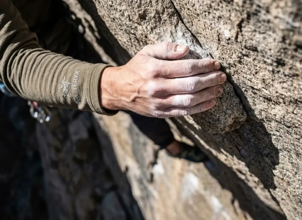 Close up of a climber's hand gripping a rock hold tightly while wearing an Arc'teryx hoody.