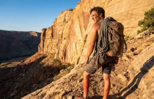 The Climber’s Pact: A Practical Field Guide A climber hiking on a desert trail with a rope backpack, looking up at red sandstone cliffs during sunrise.