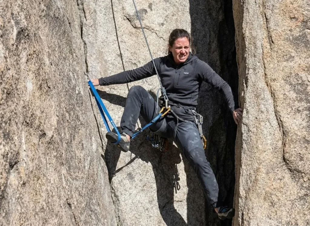 Climber wearing Patagonia gear performing a sit-stand ascent using nylon runners and standard carabiners.