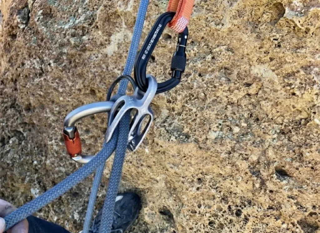 Macro close-up of a Petzl Connect Adjust and Black Diamond ATC setup, showing the proper extension configuration and material textures.
