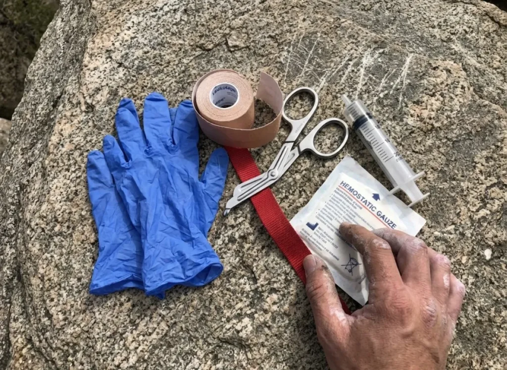A climbing first aid kit spread out on a rock, featuring trauma shears, tape, gloves, and gauze.