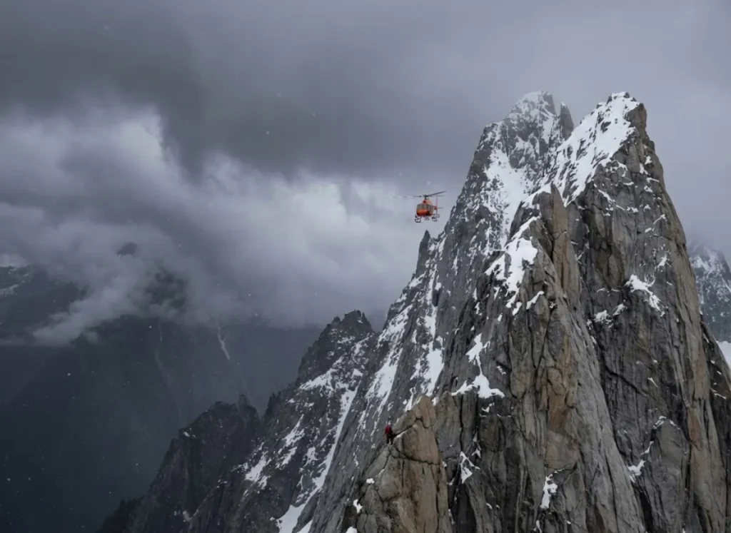 A search and rescue helicopter hovering near a steep mountain ridge, visualizing the high cost and necessity of rescue insurance.