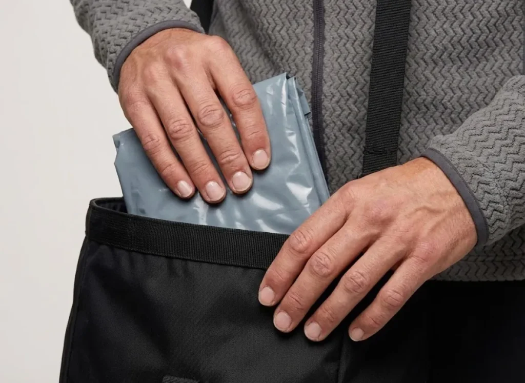 Close-up of clean hands packing a WAG bag into a Black Diamond climbing backpack, emphasizing waste management as part of technical gear preparation.
