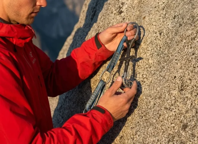 resling-cams-safely-guide Professional climber wearing an Arc'teryx jacket inspecting a Black Diamond Camalot at the base of a granite cliff during golden hour.
