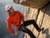 Safe Rope Ascent & The 60-Second Transition Matrix A climber wearing an Arc'teryx jacket and Petzl helmet ascending a fixed rope in free space below a rock roof.