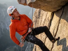 Safe Rope Ascent & The 60-Second Transition Matrix A climber wearing an Arc'teryx jacket and Petzl helmet ascending a fixed rope in free space below a rock roof.
